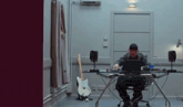 a man sits at a desk with a laptop and a guitar that says fender