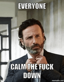 a man in a suit and tie with a beard is making a funny face and says `` everyone calm the fuck down '' .