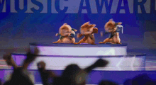 three chipmunks dancing on a stage in front of a music award sign