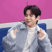 a young man is sitting on a blue couch with his eyes closed and making a heart shape with his hands .