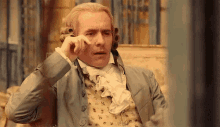 a man in a historical suit is sitting on a couch and rubbing his eye .