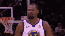 a man in a golden state warriors jersey stands in front of a basketball hoop .