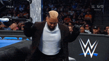 a man in a suit stands in front of a wrestling ring
