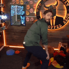a man in a green shirt is squatting in front of a sign that says the hang shop coffee