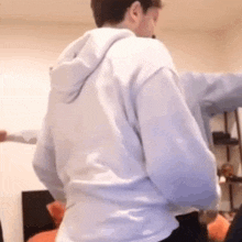 a man in a white hoodie is dancing in a room with his arms outstretched .