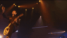 a man playing a guitar in front of a large screen that says d