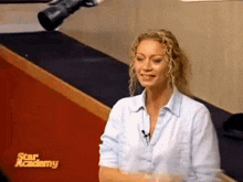 a woman in a blue shirt is sitting in front of a camera with the word star academy on the screen .