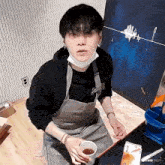 a young man wearing an apron is sitting at a table holding a cup of tea .