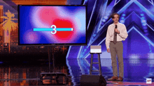 a man stands on a stage with a microphone in front of a large screen with the number 3 on it