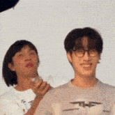 two men are standing next to each other and one of them is wearing glasses and a white shirt .