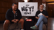 two men are sitting in front of a sign that says hey