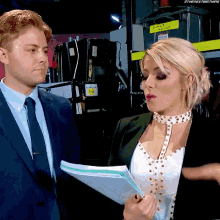 a man in a suit and tie stands next to a woman in a choker holding a piece of paper .