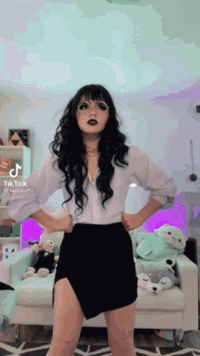 a woman in a white shirt and a black skirt is standing in front of a couch .