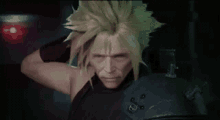 a man with blonde hair is standing in a dark room with his hand on his head .