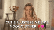 a woman is sitting in a chair and saying `` cutie flusters me like noooo other '' while holding a heart .