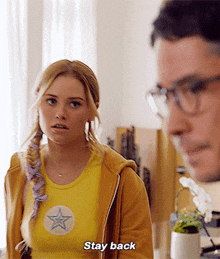 a woman in a yellow shirt with a star on it says " stay back "