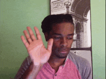 a man in a pink shirt is waving his hand in front of a picture on the wall .