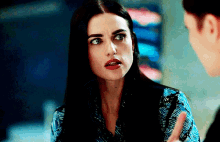 a woman with long black hair is talking to another woman while wearing a blue top .