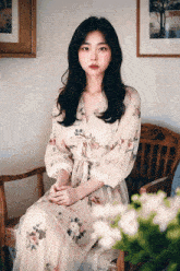 a woman wearing a floral dress sits in a chair