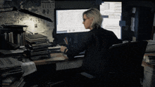 a woman sits in front of a computer with a wanted poster on the wall above her