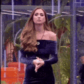 a woman in a black off the shoulder dress is standing with her hands folded .