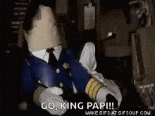 a mascot with a paper bag on his head is sitting in a chair and says `` go , king papi ! ''