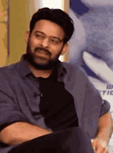 a man with a beard is sitting down with his arms crossed and making a funny face .