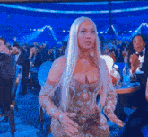 a woman in a gold dress stands in front of a crowd of people