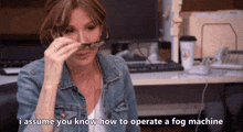 a woman wearing glasses and a denim jacket is talking about how to operate a fog machine