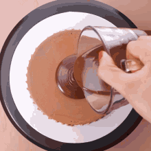 a person pouring chocolate into a cake with a glass