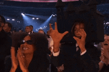 a man and a woman are clapping in a crowd while wearing sunglasses