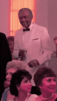a man in a white tuxedo stands in front of a crowd of people