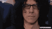 a man with black hair and glasses is making a funny face .
