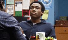 a man is sitting at a table with a sandwich and a mug with a picture of a man on it