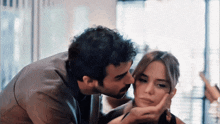 a man kisses a woman on the cheek while she holds her hand to her face