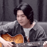 a young man with long black hair is playing an acoustic guitar with signatures on it .
