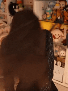 a woman wearing a black sweater and a black skirt is standing in front of a shelf filled with stuffed animals .