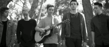 a group of young men are standing next to each other one of them is holding a guitar