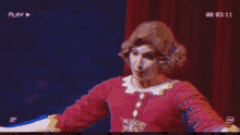 a man in a red dress is on a stage with a play button on the bottom