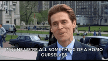 a man in a suit and tie says in june we 're all something of a homo ourselves in front of a car .