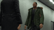a man in a green parka is talking to another man in a suit .