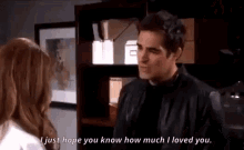 a man and a woman are standing next to each other in a room . the man is wearing a black leather jacket .
