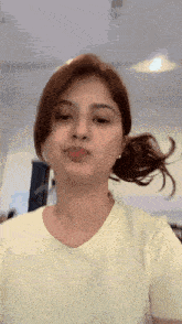 a woman in a yellow shirt is making a funny face with her hair in a ponytail .