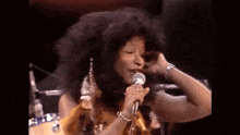 a woman singing into a microphone with a drum set in the background