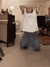 a man in a white shirt is kneeling down in a living room with his hands on his head .