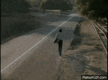 a man is standing on the side of a road near train tracks .