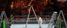 a man in a white suit is standing in a wrestling ring with a crowd watching .