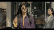 a woman wearing sunglasses and a purple coat is walking down a street