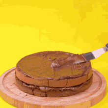 a chocolate cake is being spread with a spatula on a wooden cutting board