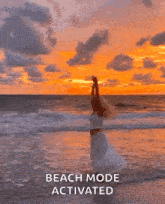 a woman in a white dress is standing on a beach at sunset with her arms in the air .